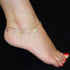 A close-up shot features a foot adorned with the exquisite Mega Lucky Charm Anklet Bracelet, showcasing five amulets for good luck, including an evil eye charm for protection, set against a black background. The toenails are painted red.